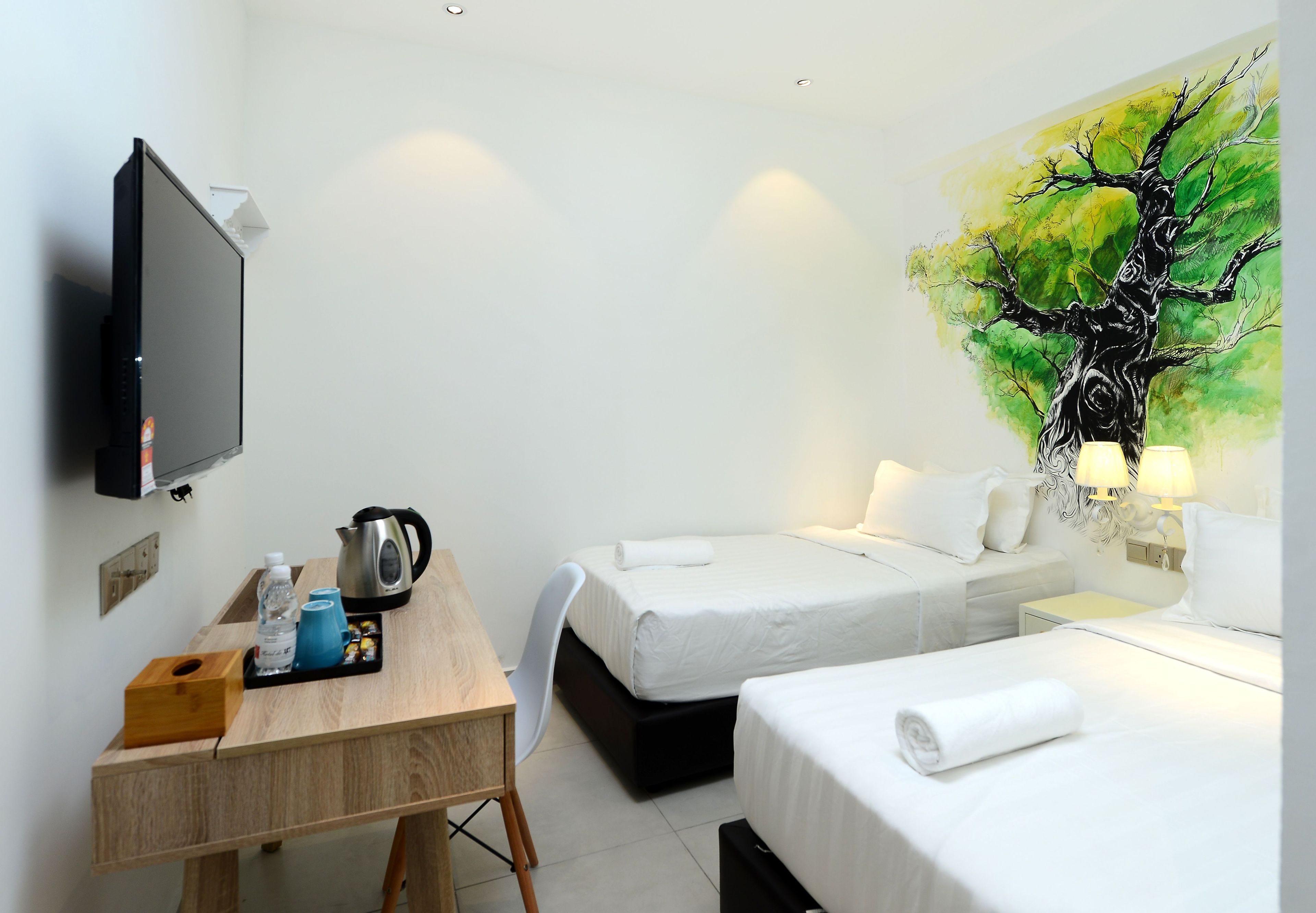 Une chambre d’hôtel avec un bureau, deux lits, un tableau représentant un arbre et un téléviseur fixé au mur.