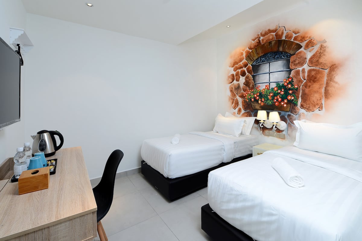 Une chambre d’hôtel avec deux lits, un bureau, une machine à café et un mur décoratif agrémenté d’une fausse cheminée.