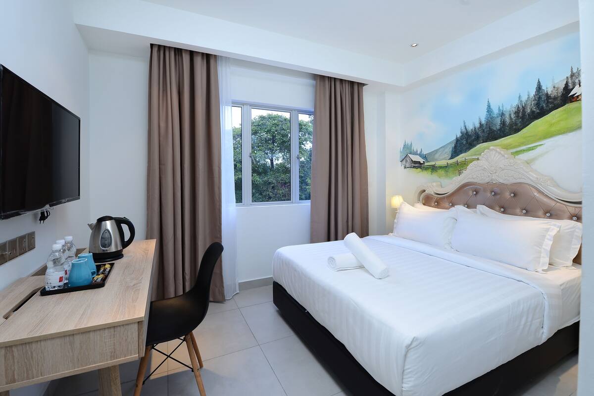 Une chambre d’hôtel avec un lit, un bureau doté d’une bouilloire, une télévision et un tableau représentant un paysage.