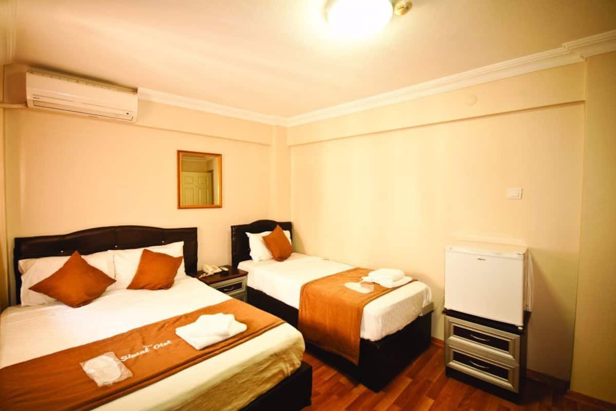 A hotel room with two beds, a small refrigerator, and an air conditioning unit.