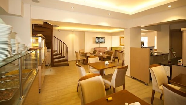 En hotels restaurant med borde og stole, et buffetbord med tallerkener, og en trappe til en anden etage.