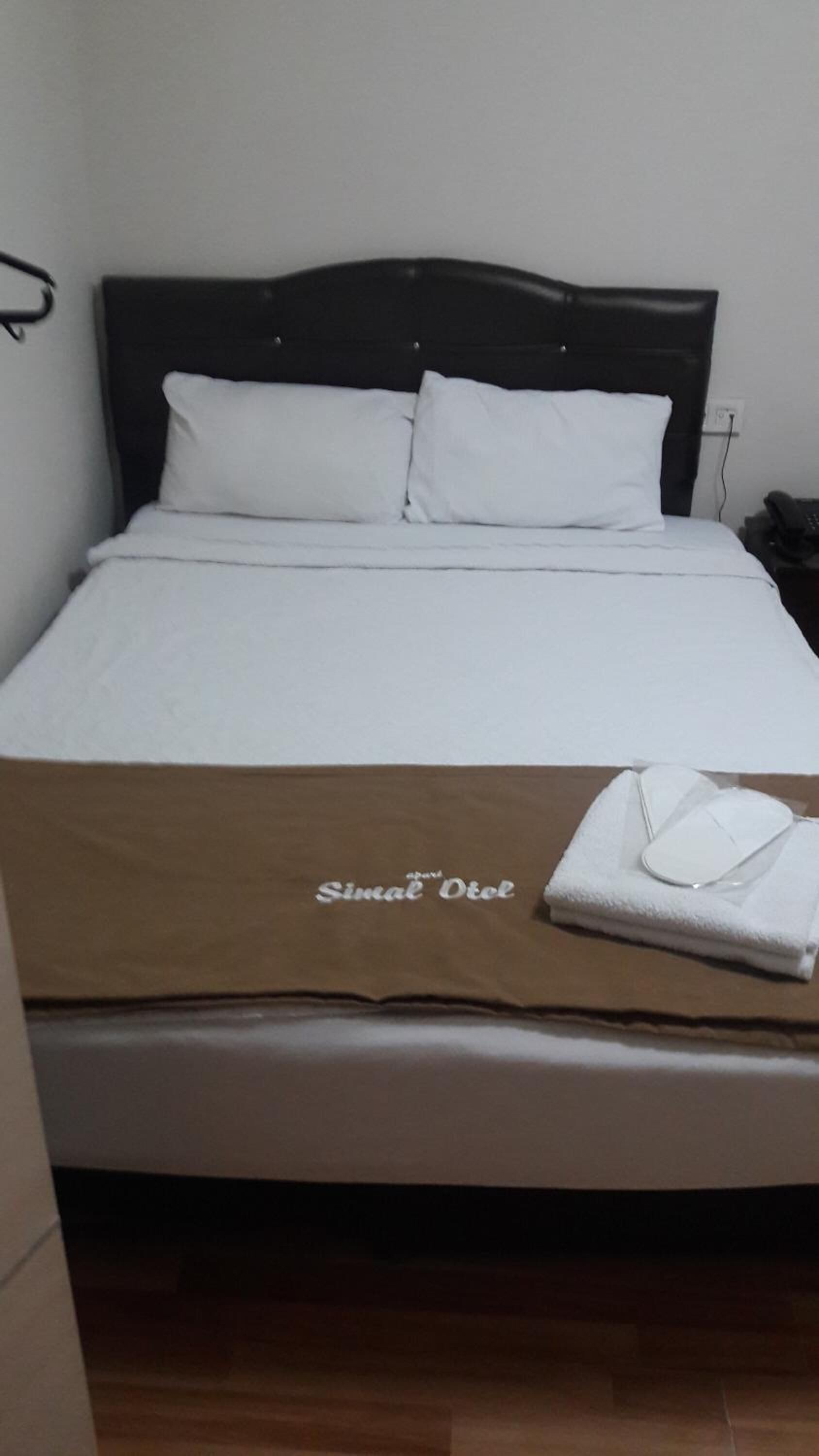 A bed with a headboard, white bedding, and a brown blanket with text.