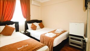 Et hotelværelse med to senge, brunt sengetøj, et hvidt natbord, et hvidt fjernsyn og en aircondition på væggen.