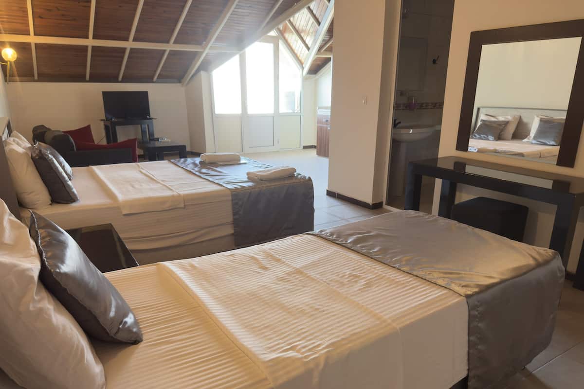 Habitación de hotel con dos camas, un escritorio, un televisor y un baño visible a través de una puerta abierta.