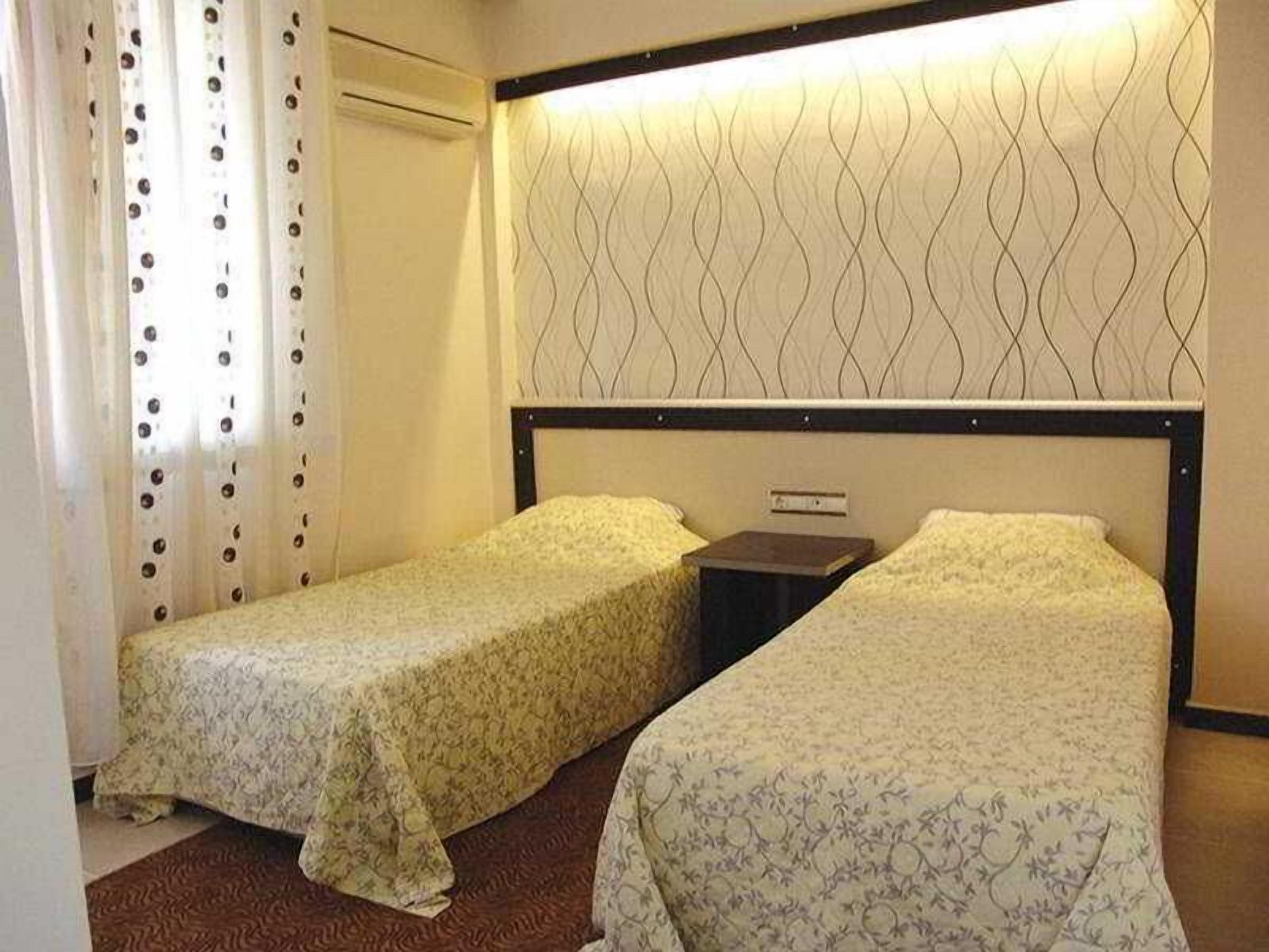 Quarto de hotel com duas camas de solteiro, mesa de cabeceira, ar condicionado fixado na parede e cortina estampada.
