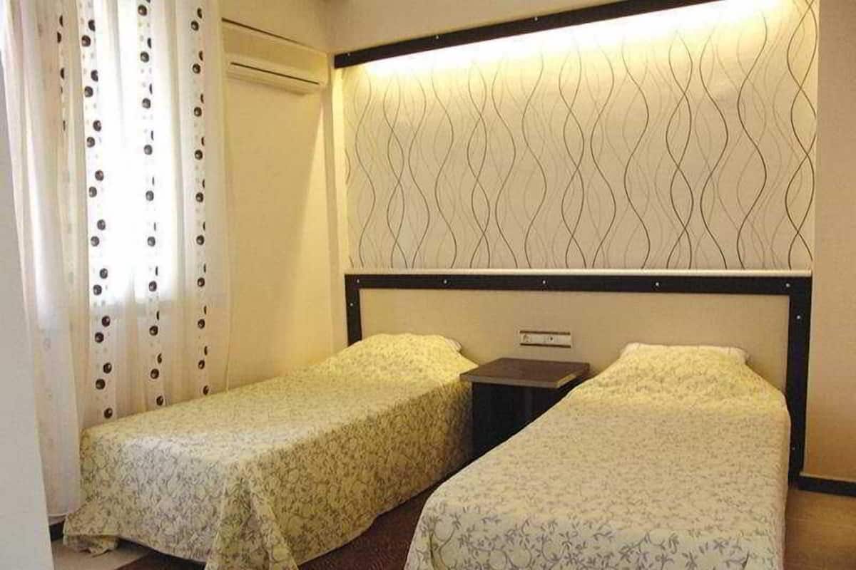 Una habitación de hotel con dos camas individuales, una mesita de noche, un aire acondicionado de pared y una cortina estampada.