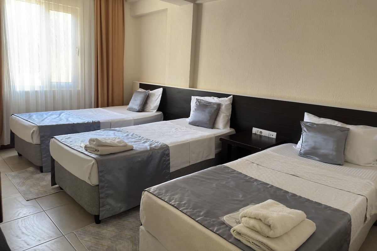Habitación de hotel con dos camas individuales, una mesita y un ventanal con cortinas.