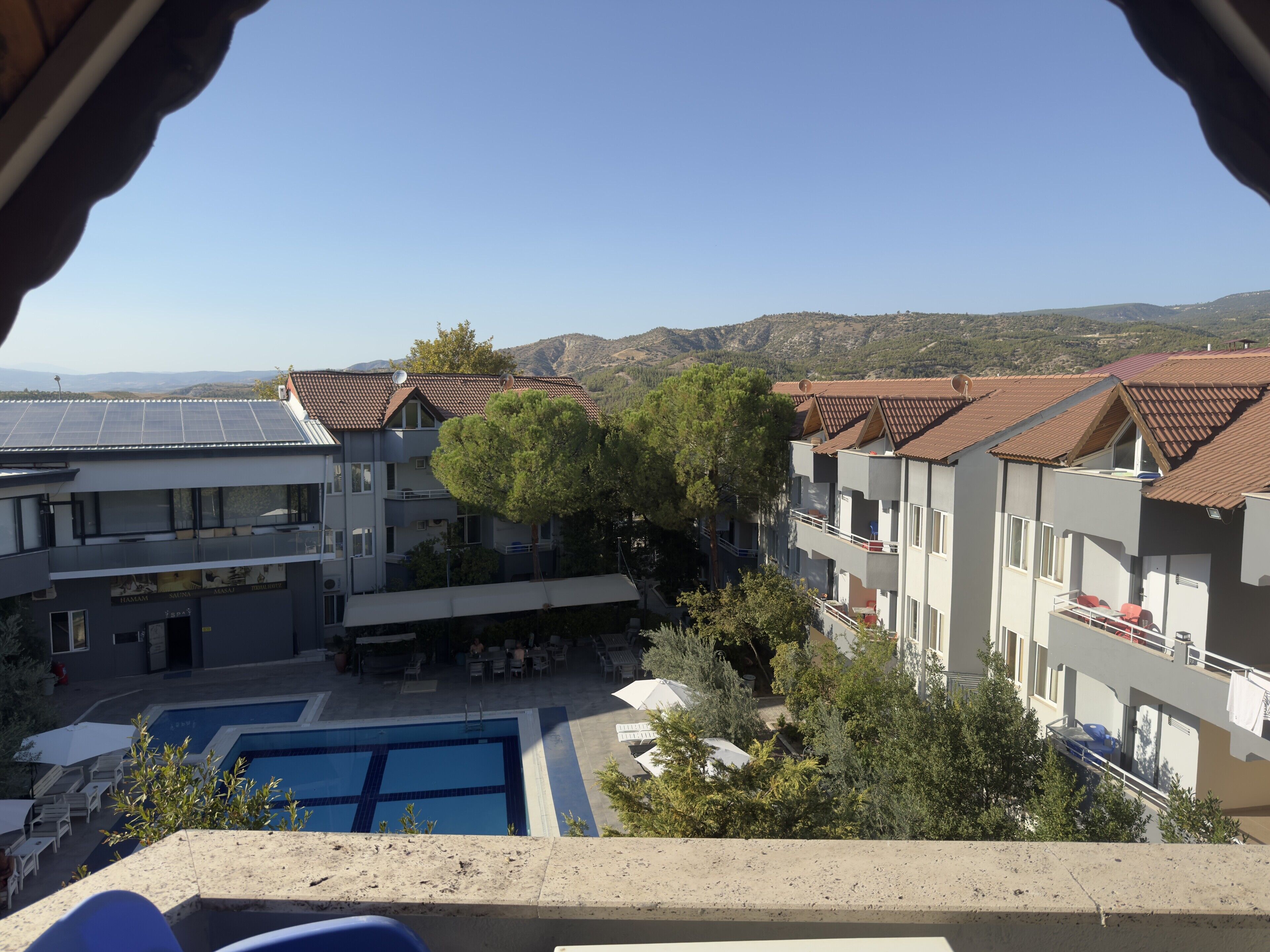 Um hotel com piscina, várias varandas e vista para as colinas ao redor.