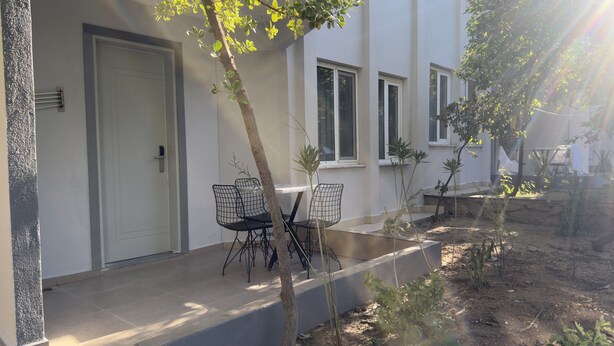 Un patio con una mesa, sillas, una puerta y un árbol pequeño.