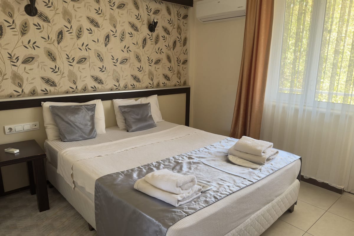 Una habitación de hotel con una cama grande, una mesita de noche y una ventana con cortinas.