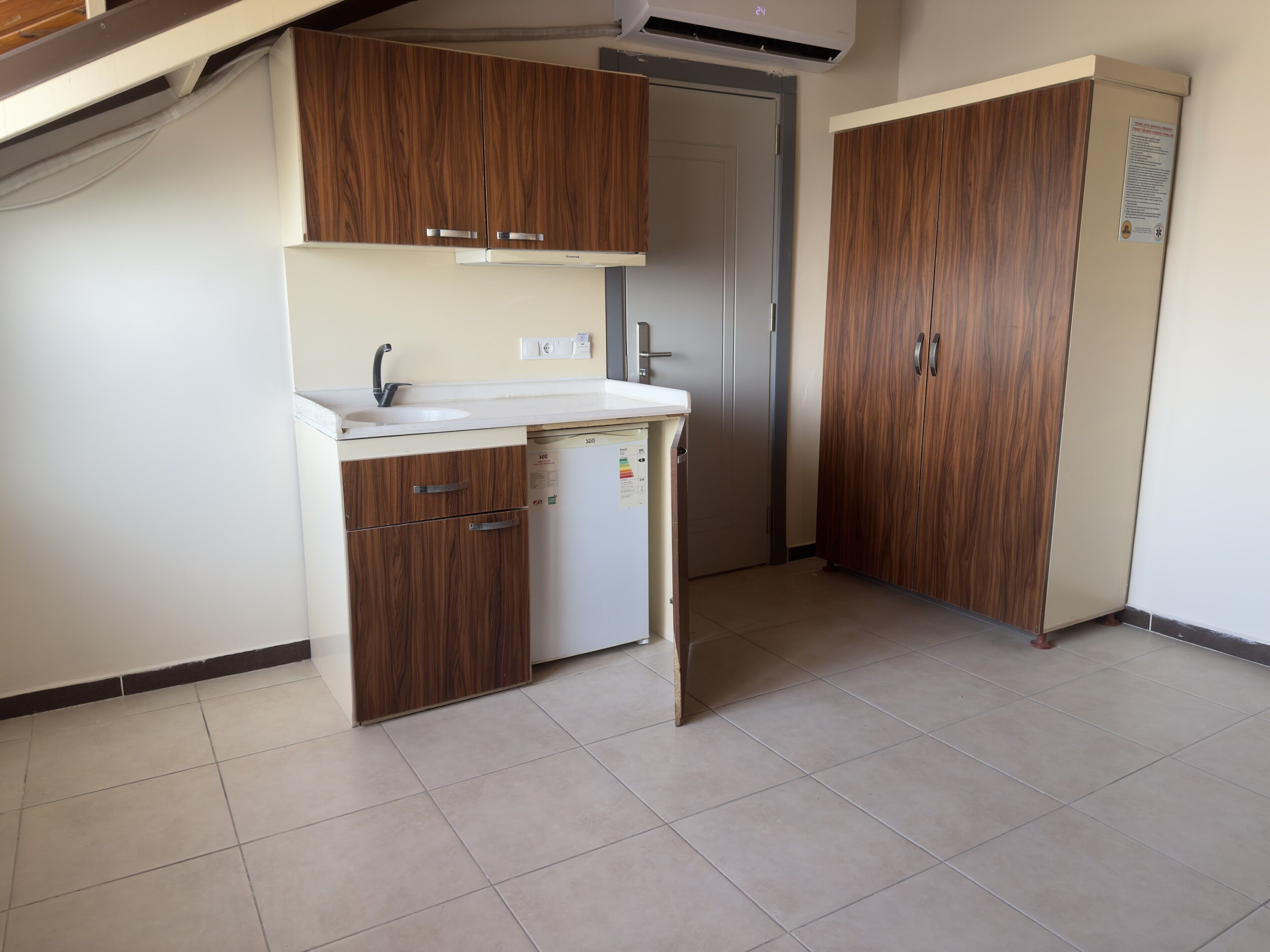 A compact kitchen with wooden cabinets, a white sink, and a small refrigerator.