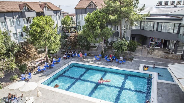 A swimming pool with lounge chairs and umbrellas, surrounded by trees and buildings.