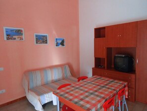 A small, cozy room with a sofa, a table, and a TV cabinet. - Appartamenti Sul Porticciolo (Castelsardo)