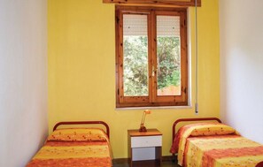 A room with two beds, a window with shutters, and a small bedside table with a lamp. - Appartamenti Sul Porticciolo (Castelsardo)