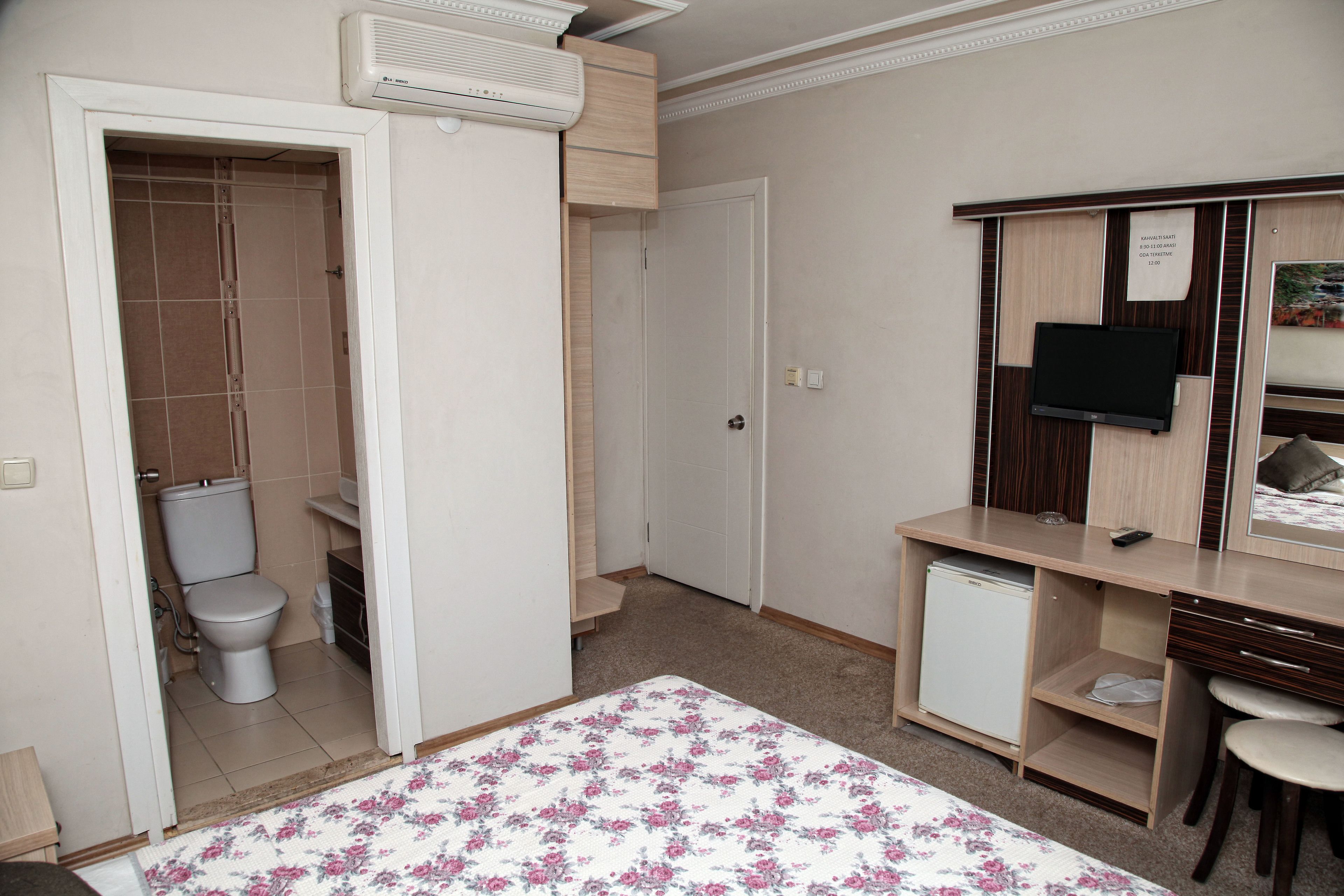 A small, neatly organized room with a bed, a desk, a chair, a television, and a small refrigerator.