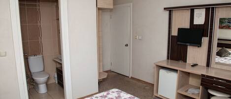 A small, neatly organized room with a bed, a desk, a chair, a television, and a small refrigerator.