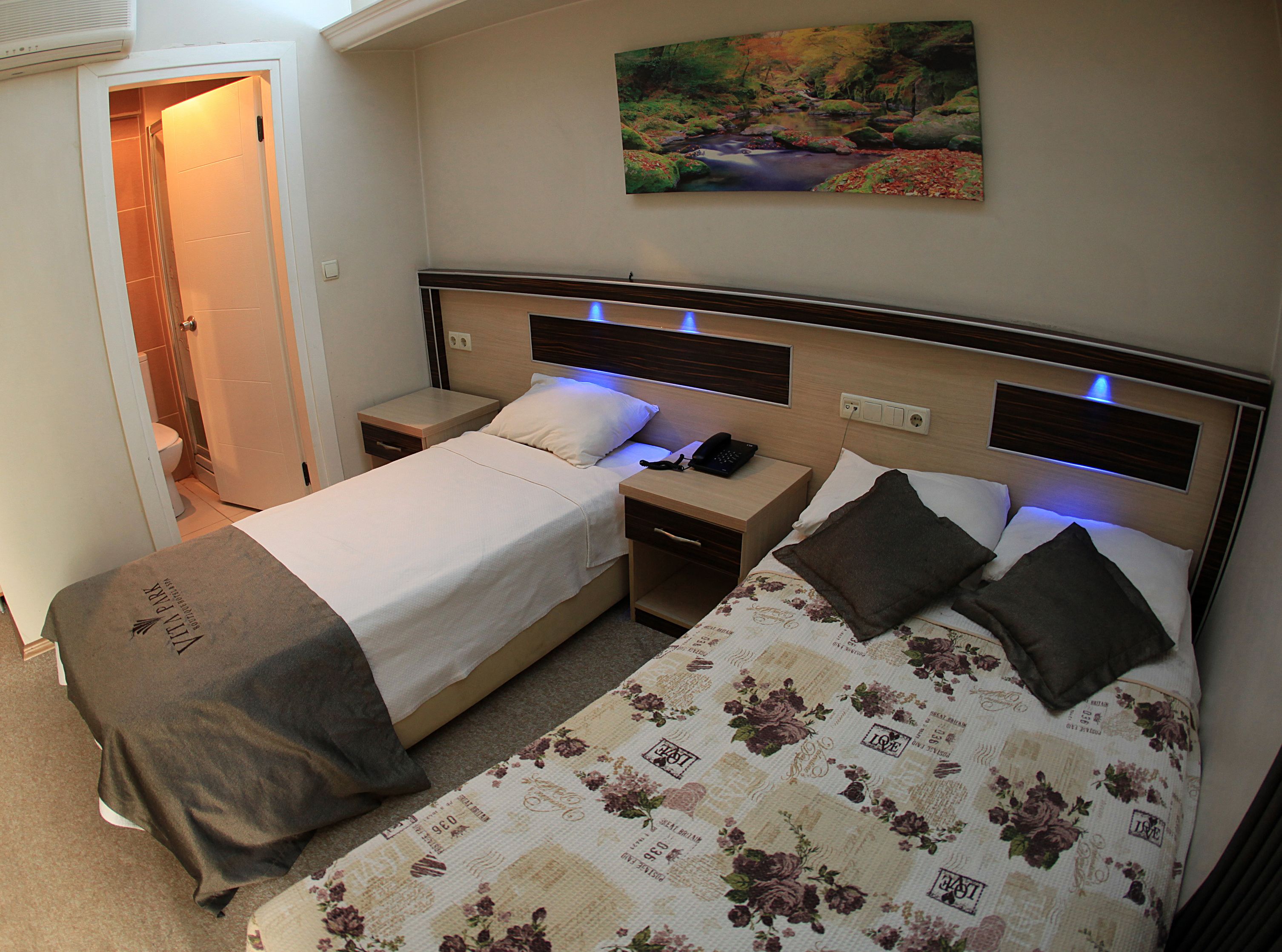 Una cama doble con edredón estampado de flores, una mesita de noche con un teléfono y una mesita con una lámpara.
