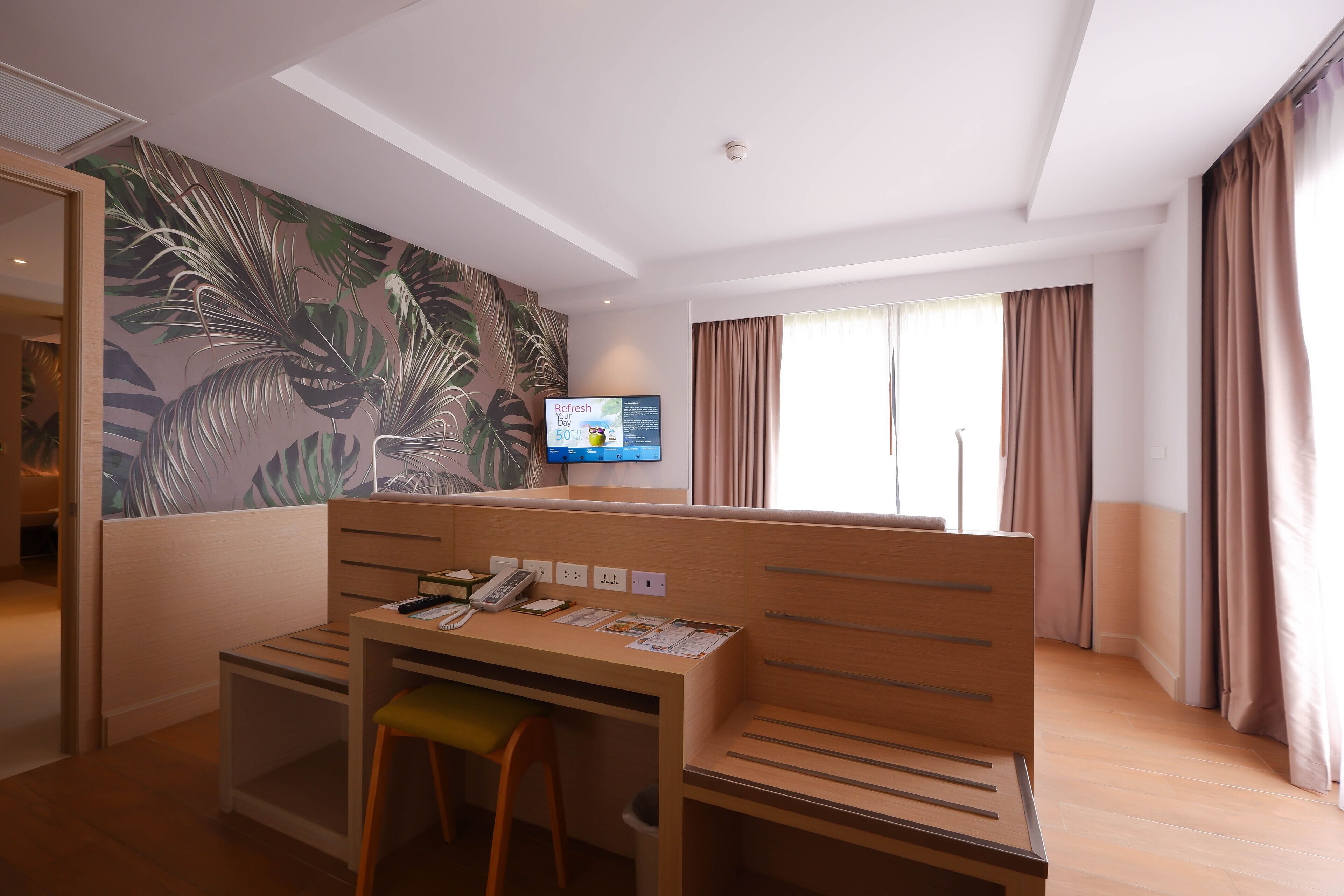 A hotel room with a wooden desk, a chair, a television, and a large window with curtains.