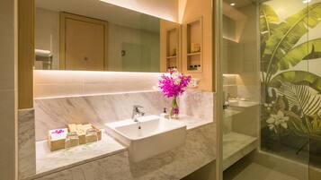 A modern bathroom with a large mirror, two sinks, marble countertops, and a shower with a tropical leaf design.