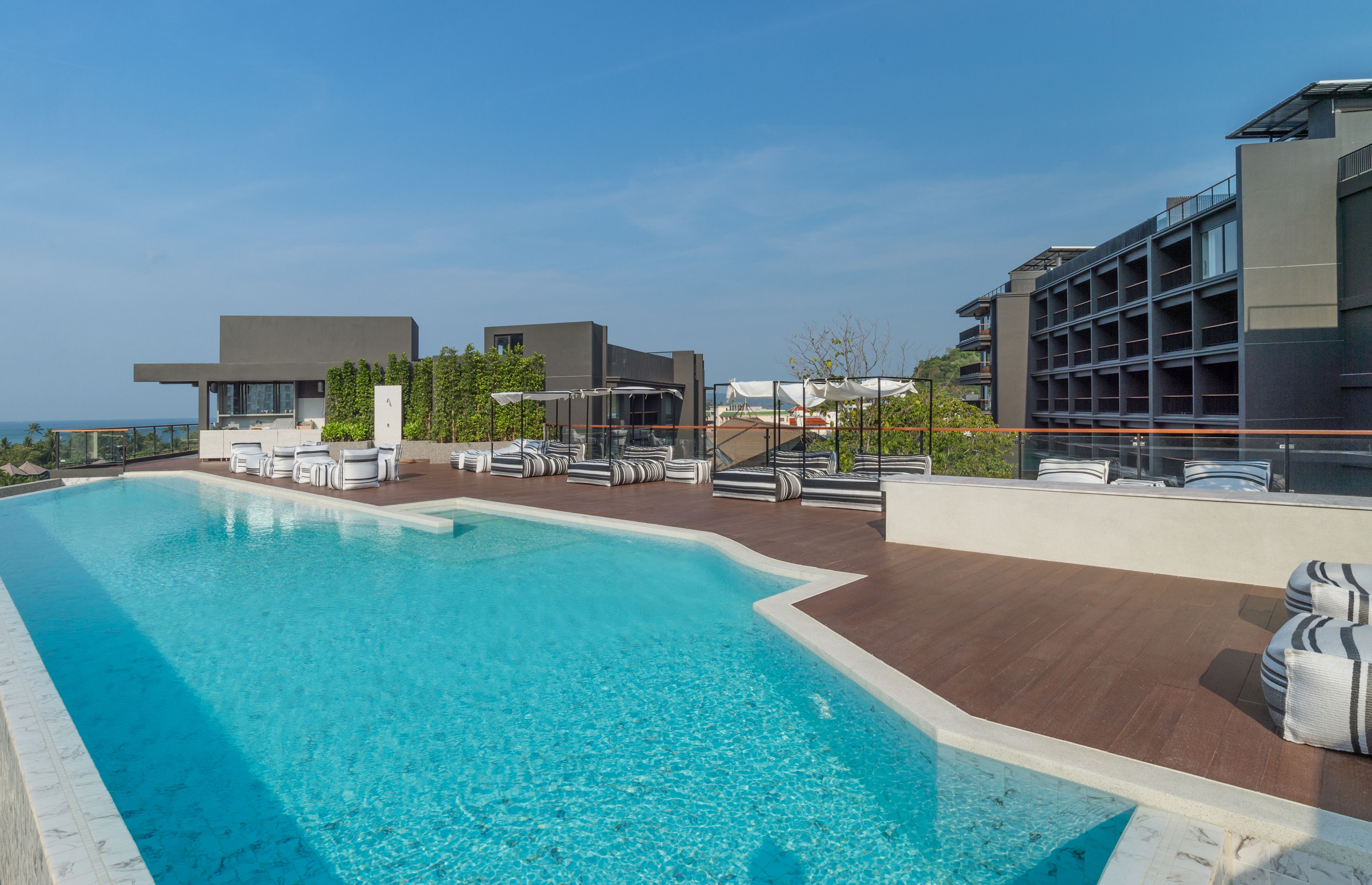 Un hotel moderno con piscina en la azotea, mobiliario exterior y vistas al océano.