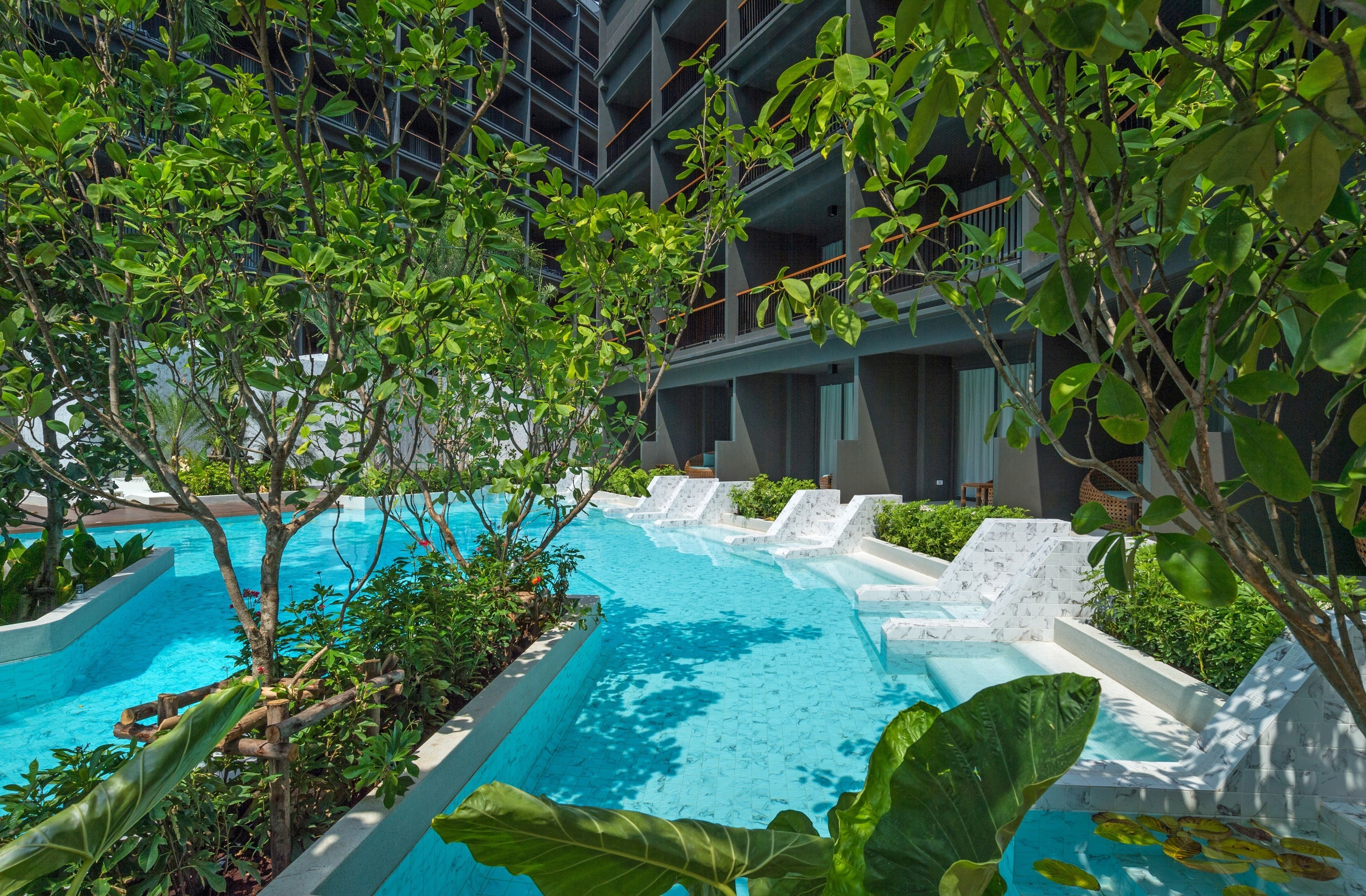 An indoor swimming pool with multiple lanes, surrounded by lush greenery and a modern building in the background.