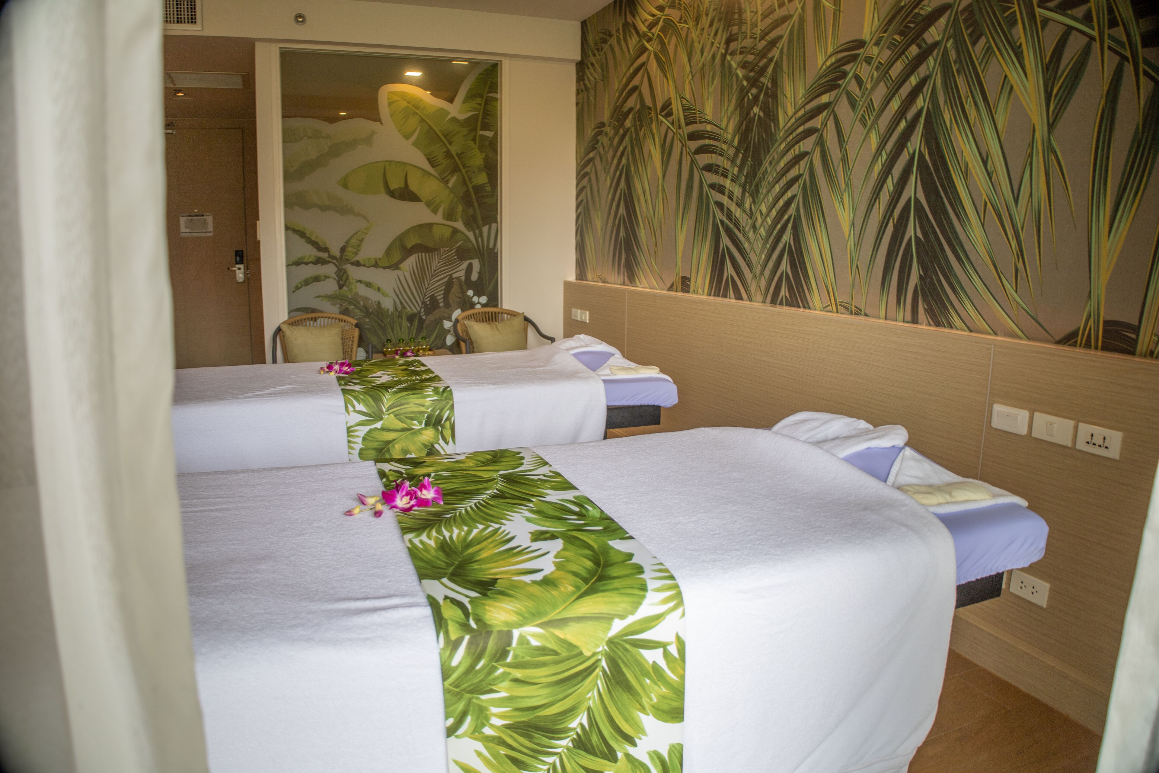 A hotel room with two beds, a large tropical-themed mural on the wall, and a wooden headboard.