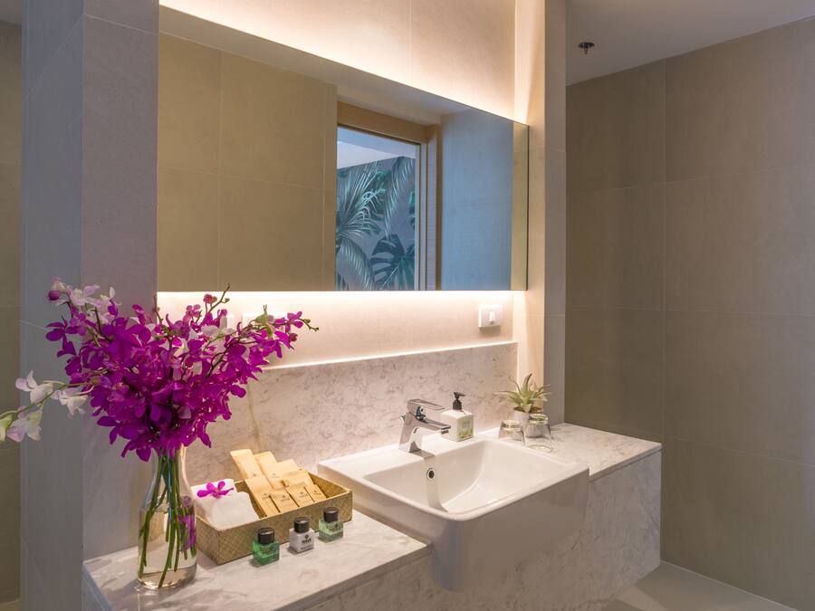 Un baño moderno con una bañera grande, un espejo sobre el lavabo y un jarrón con orquídeas moradas.