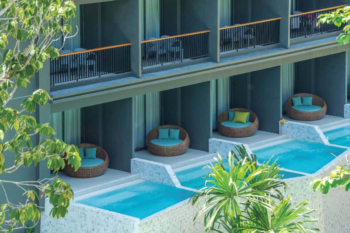A hotel with multiple balconies, each with wicker chairs and cushions, and a pool area with clear blue water.