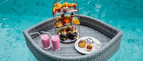 Una mesa de mimbre con comida y bebidas junto a una piscina.