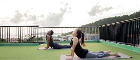 Two people doing yoga on a rooftop with a view of buildings and trees in the background.