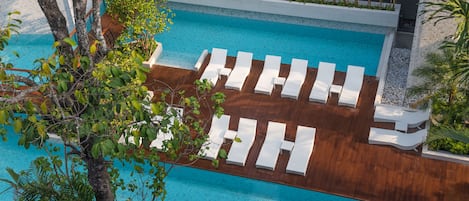 Un espace piscine agrémenté de chaises longues blanches disposées en rangées, entouré de verdure et doté d’une terrasse en bois.