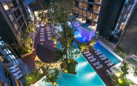 An aerial view of a hotel with multiple swimming pools, lush greenery, and modern architecture.
