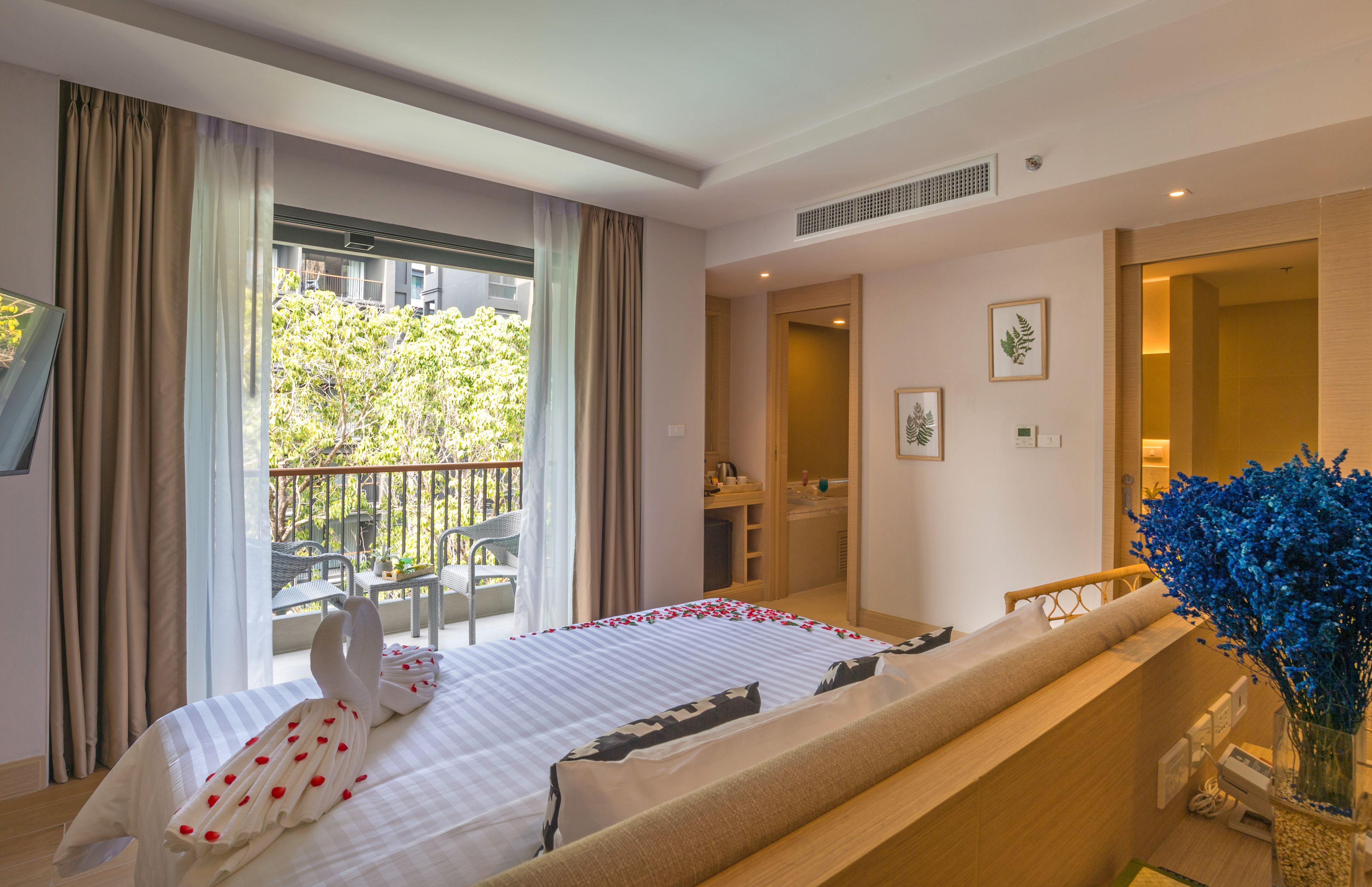 Habitación de hotel con cama, balcón, baño y vistas a la vegetación.