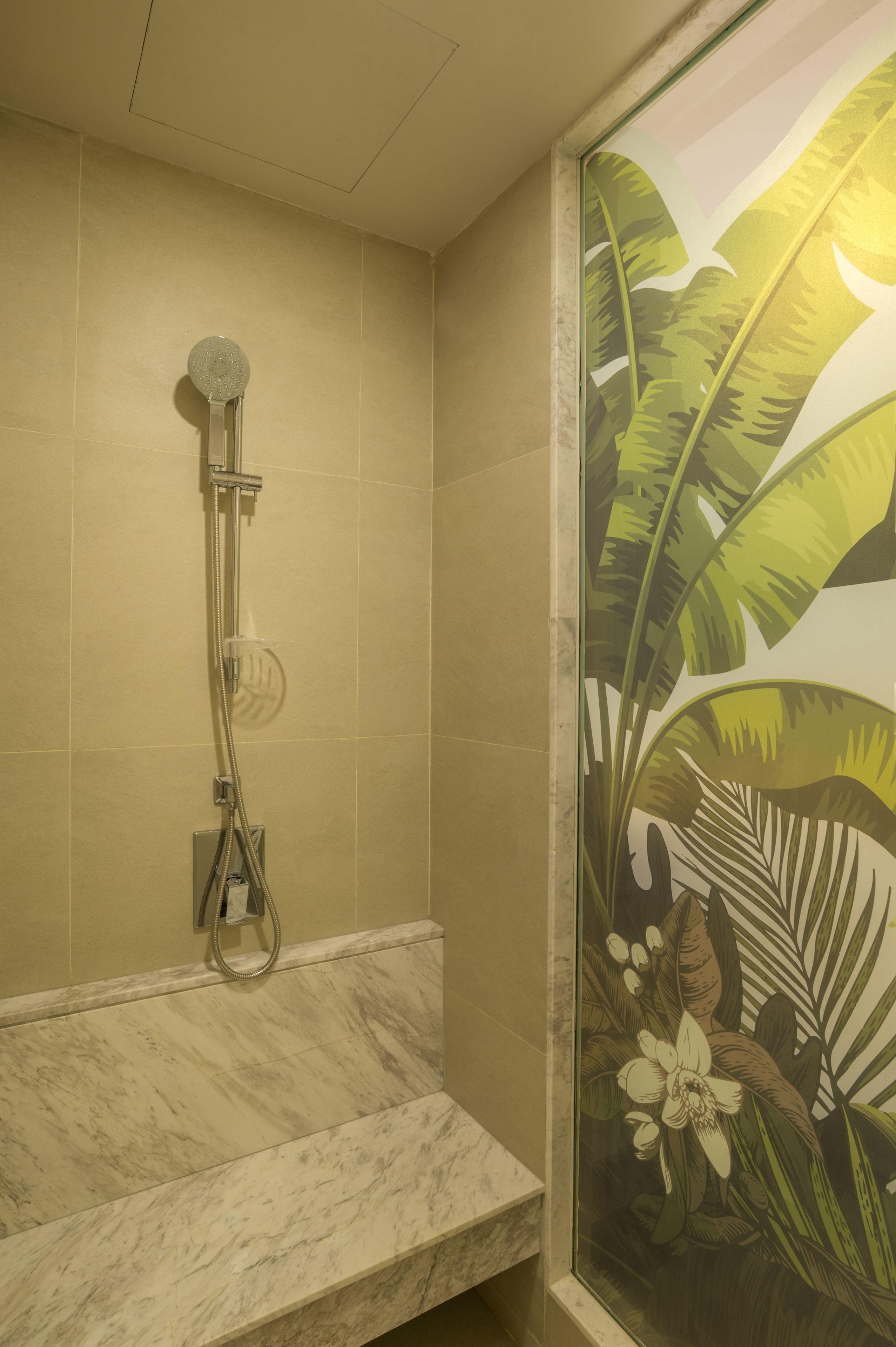 Une salle de bain avec une douche, un lavabo en marbre et un mur décoratif orné d’un motif de feuilles tropicales.