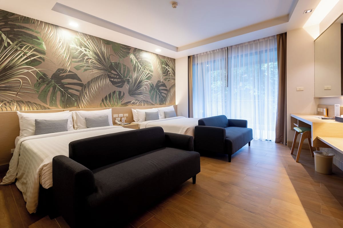 A modern hotel room with a large bed, a sofa, a desk, and a large window with curtains.