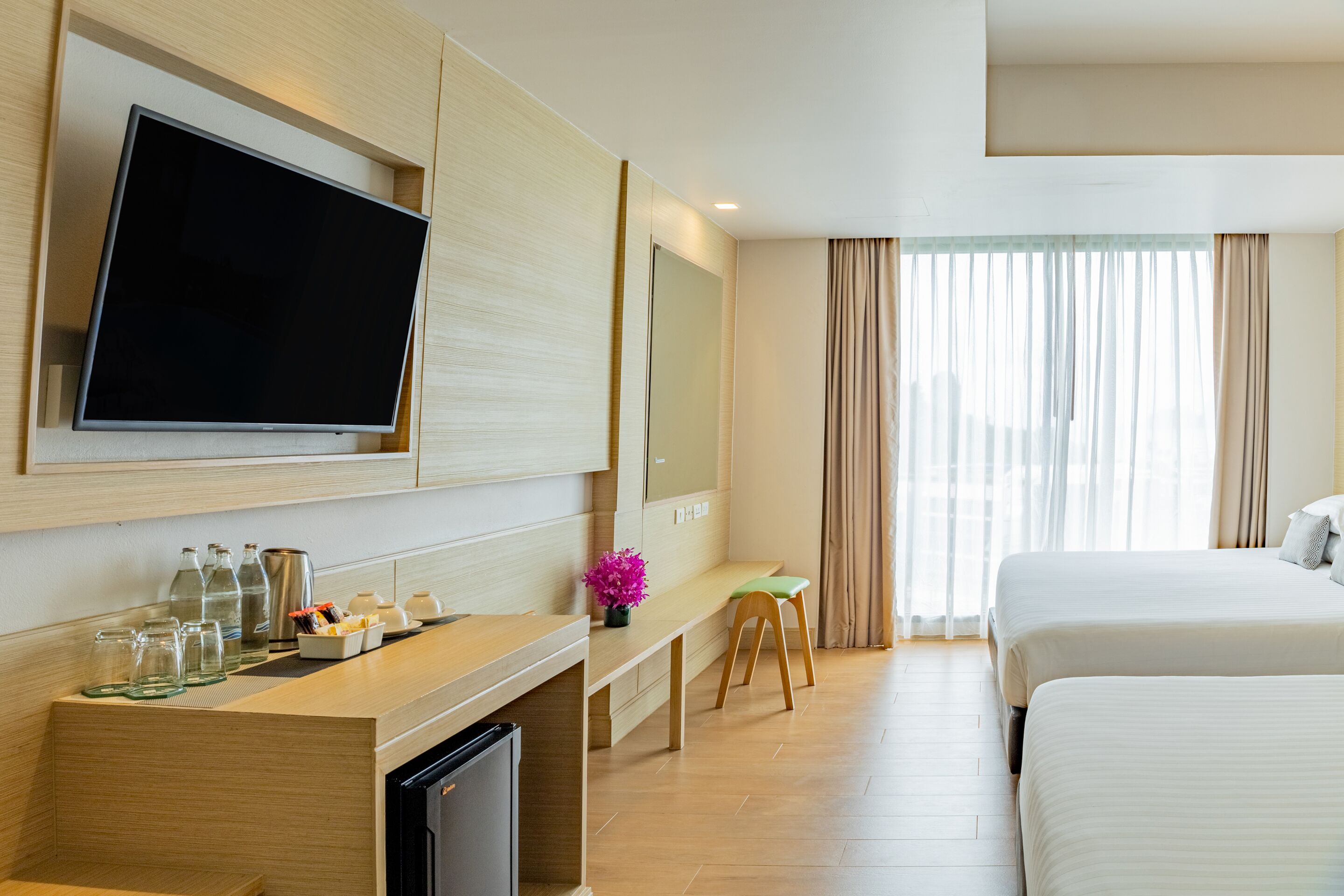 Habitación de hotel con televisión de pantalla plana, un escritorio con computadora, un taburete pequeño y dos camas.