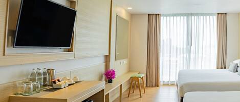 A hotel room with a flat-screen TV, a desk with a computer, a small stool, and two beds.
