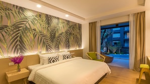 A hotel room with a large bed, a nightstand with a vase of flowers, a wall mural, a wicker chair, and a view of the outside balcony. - Panan Krabi Resort (Krabi)