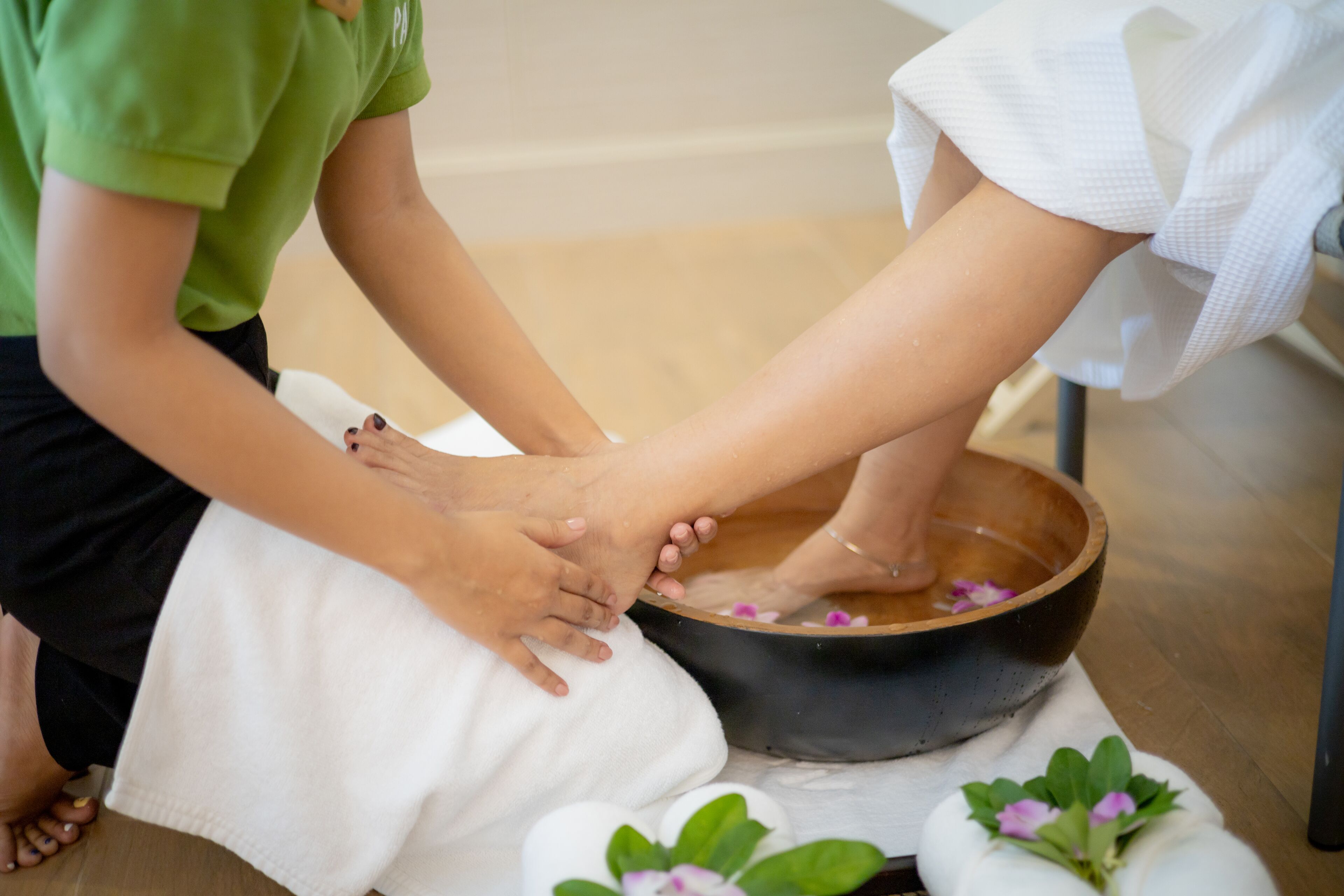 Fußmassage mit einer Holzschüssel und Blumen.
