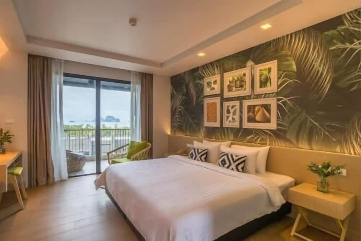 A hotel room with a bed, a nightstand, a chair, a balcony with a view, and a wall with framed pictures.