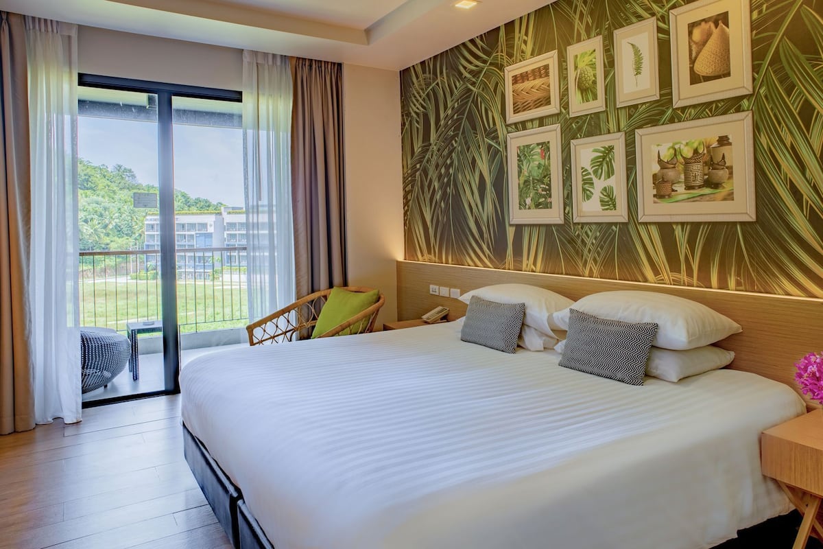 A hotel room with a large bed, a chair, a small table, a phone, and a view of the outdoors.