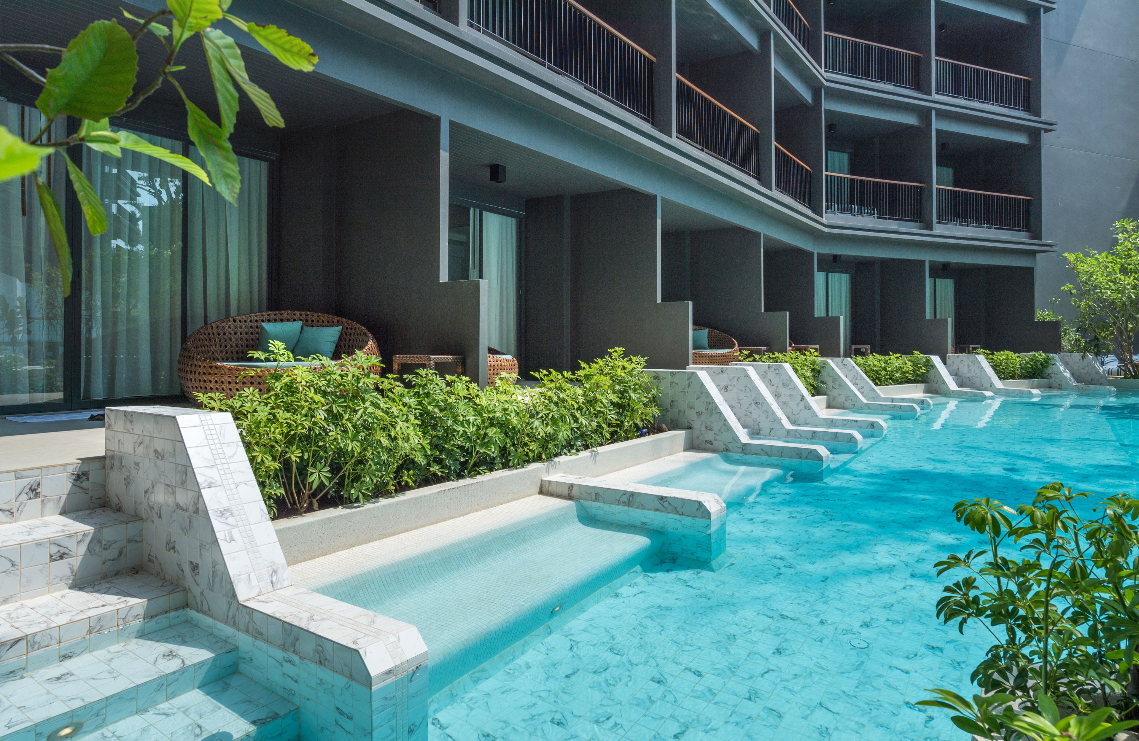 Et moderne hotel med swimmingpool, udendørs siddepladser og en høj bygning.