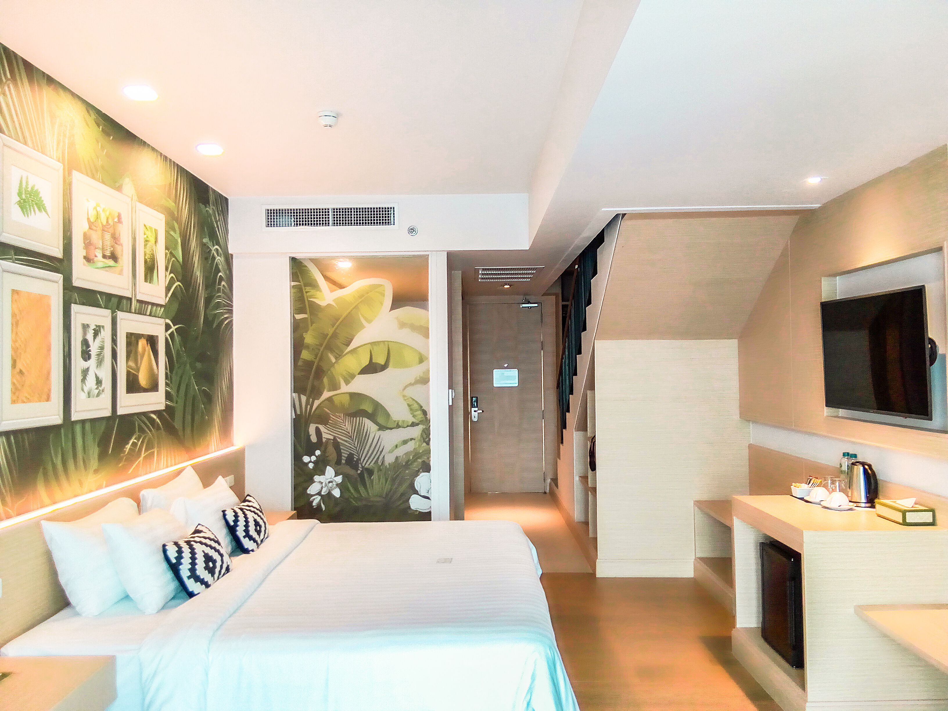 A modern hotel room with a large bed, a TV, a desk, and a wall with framed pictures.