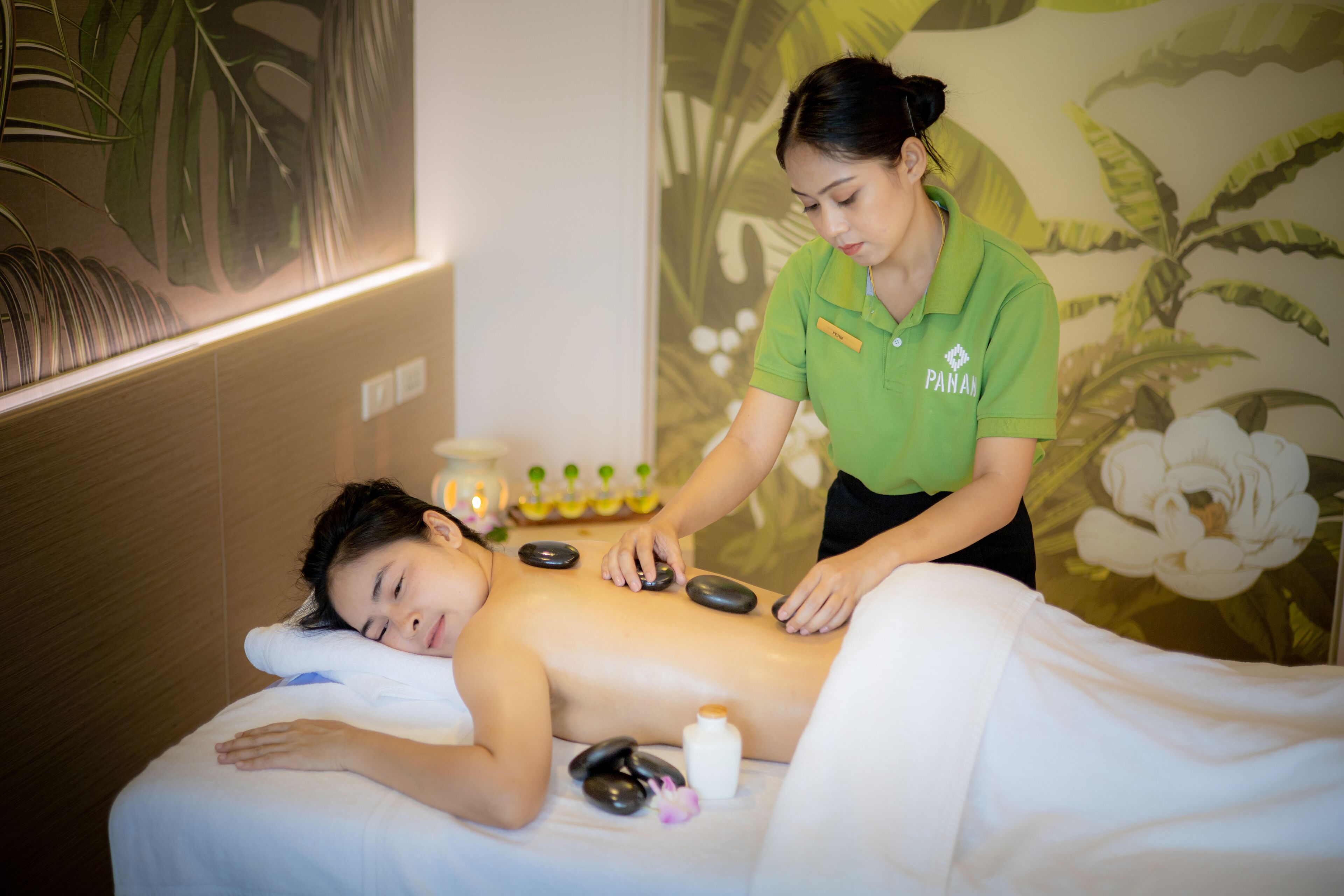 A massage therapy session in a room with a floral mural, a massage table, and a bottle of oil.
