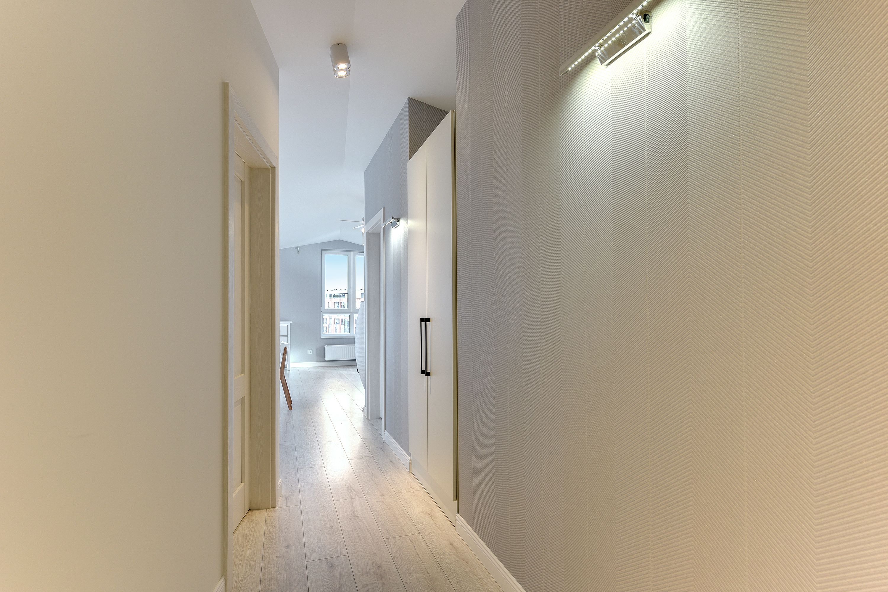 Un corridoio moderno con pavimento in legno chiaro, pareti bianche e un soffitto con illuminazione a incasso.