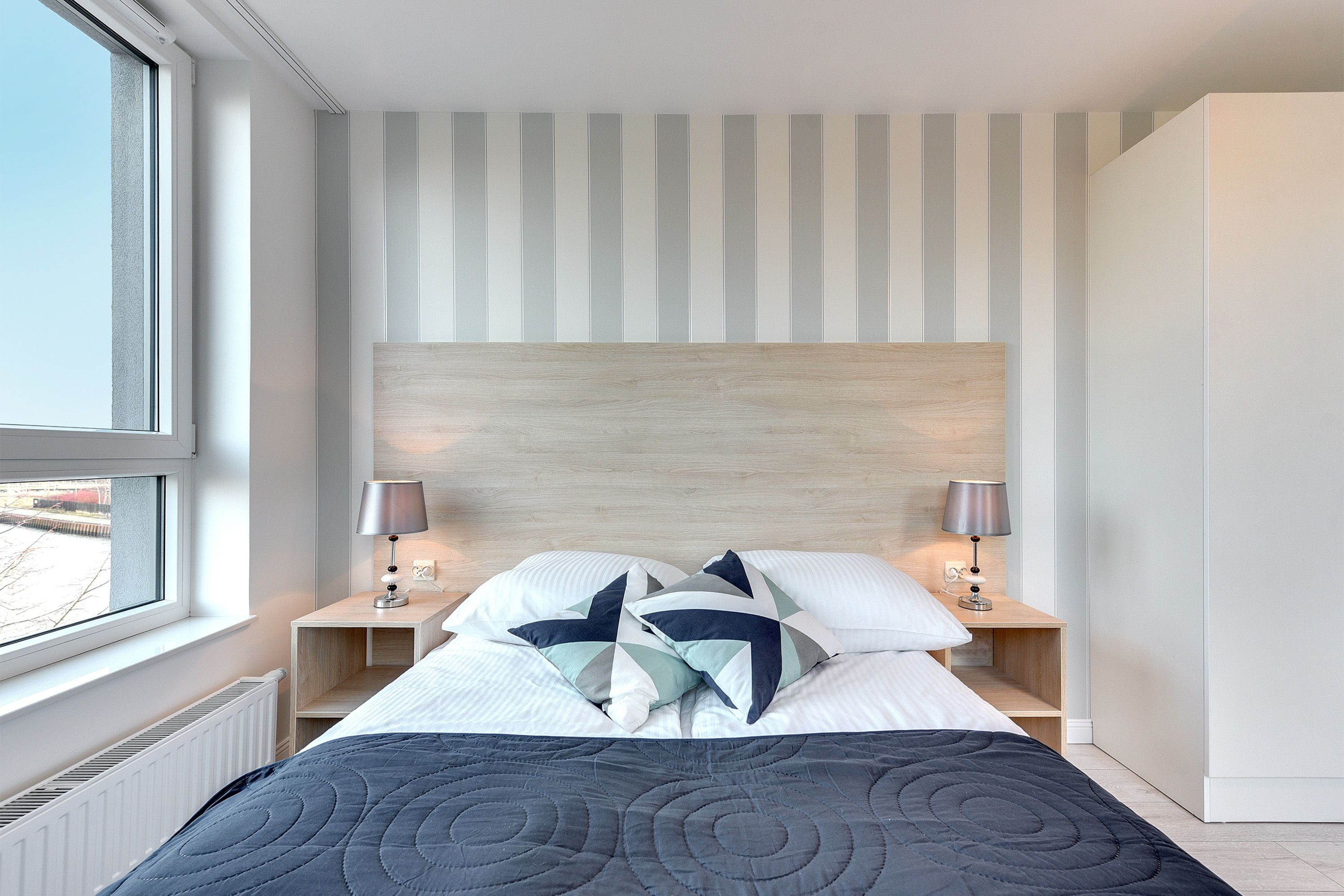 Een moderne slaapkamer met een groot bed, een gestreept accentmuur en twee nachtkastjes met lampen.