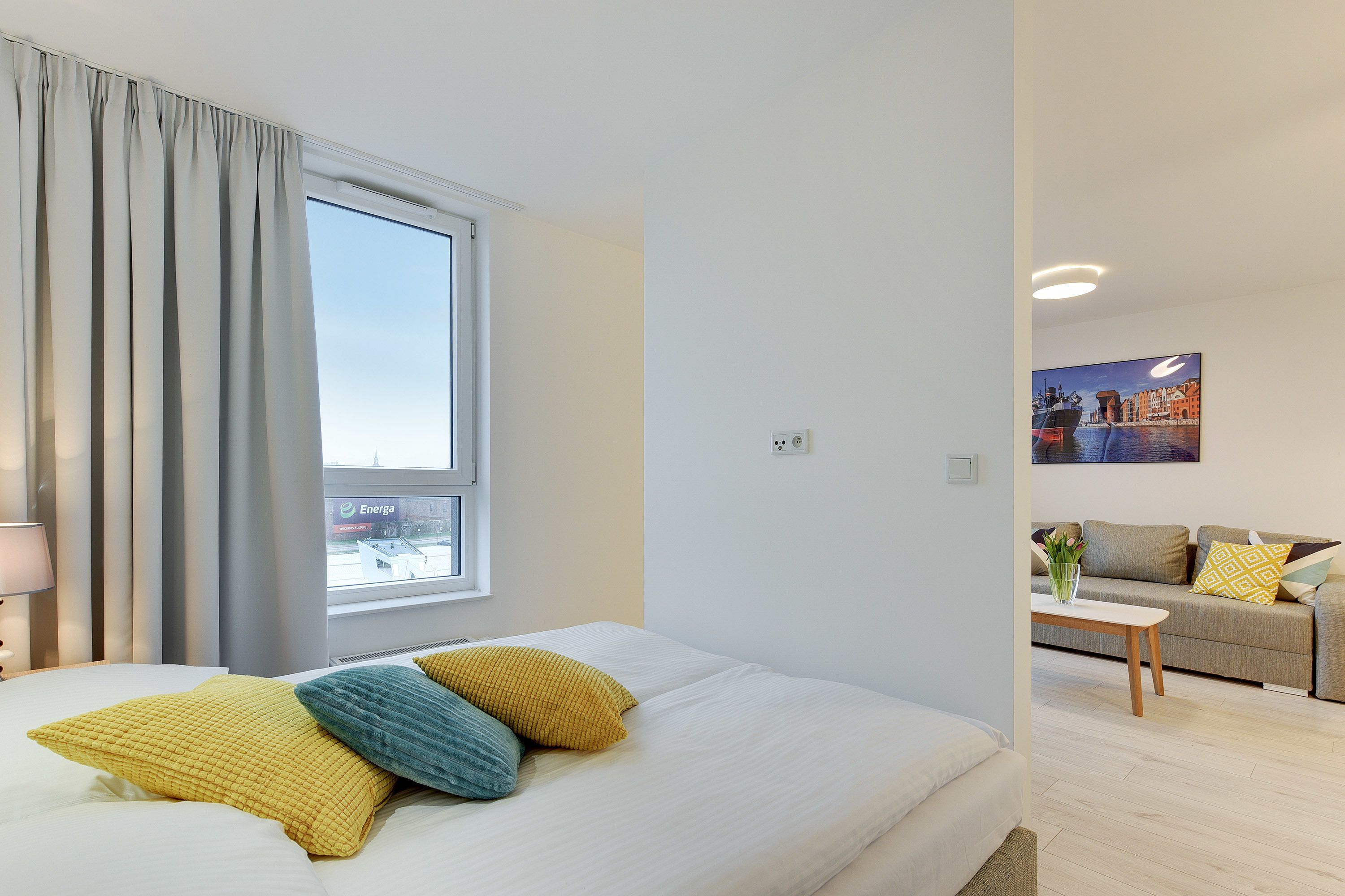 Una camera d'albergo con un letto, una finestra con tende, un divano e un quadro appeso al muro.