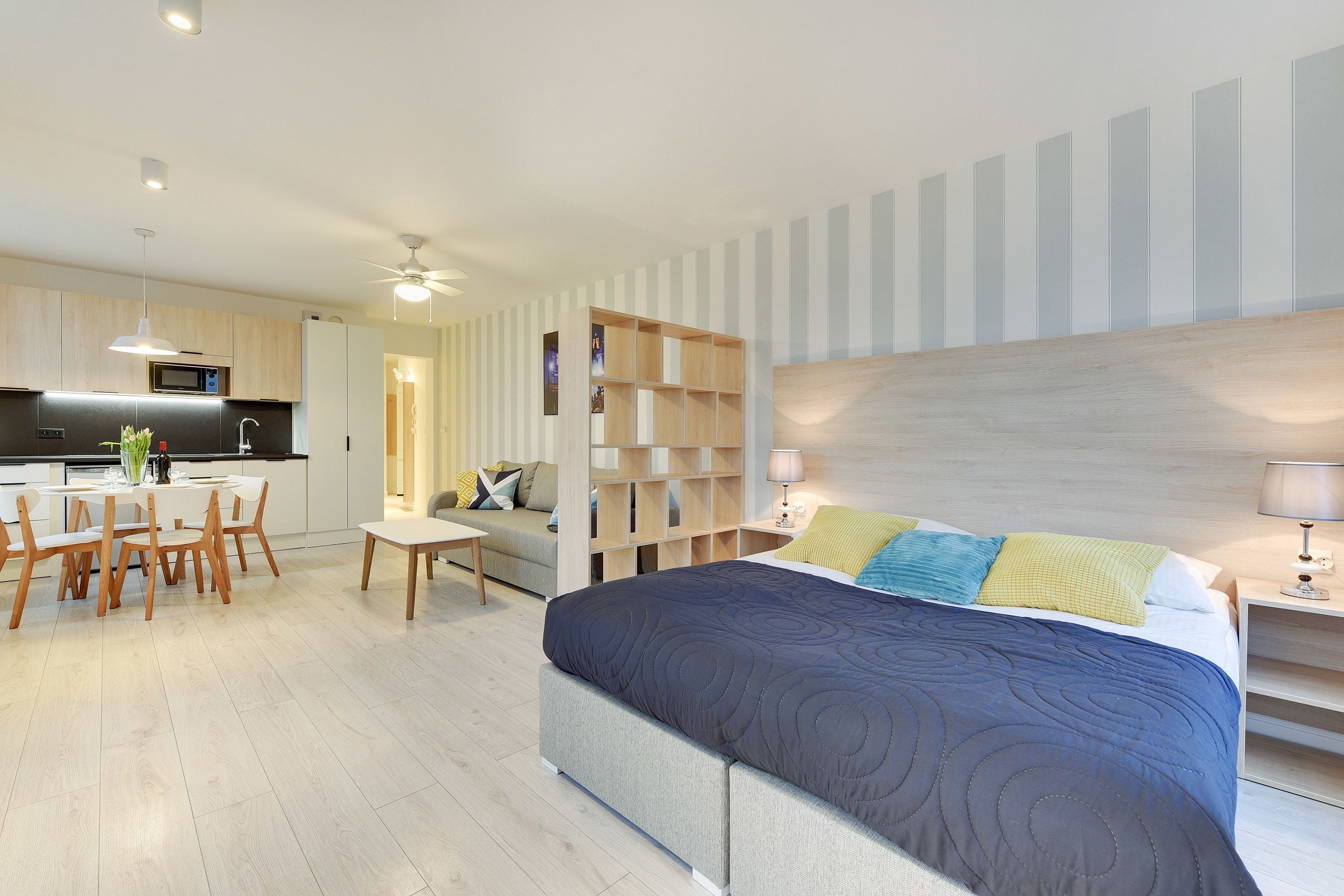 A modern hotel room with a large bed, a dining area, and a kitchenette.