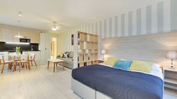 A modern hotel room with a large bed, a dining area, and a kitchenette.