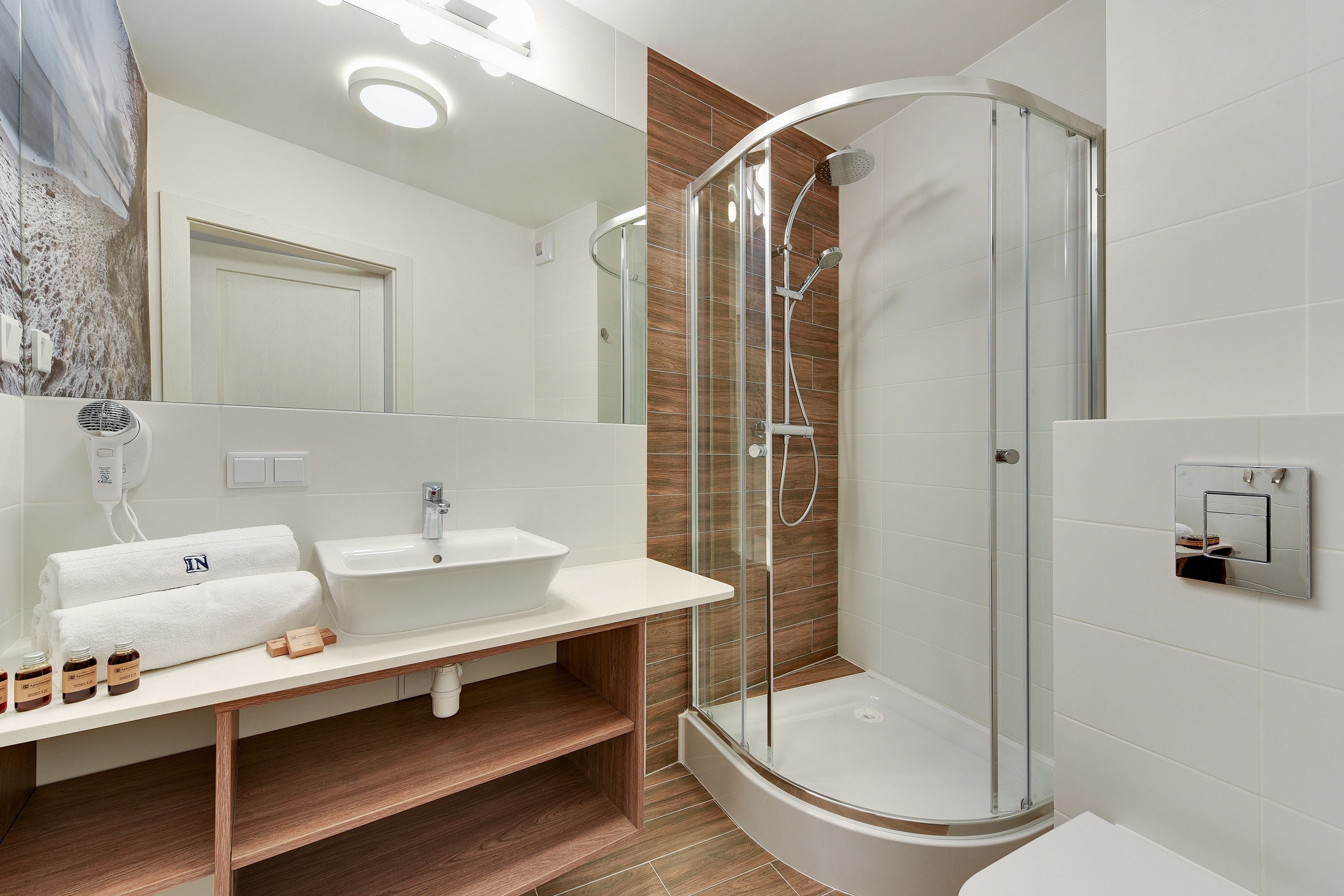 Ein modernes Badezimmer mit einer begehbaren Glasdusche, einem weißen Waschbecken und einem Holzlagerraum.